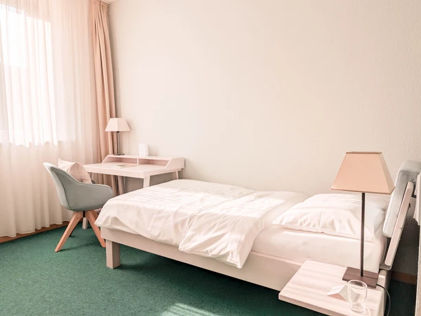 Stiftung Reformhaus Fachakademie - Ein helles Einzelzimmer mit weißem Bett Ein helles Einzelzimmer mit weißem Bett, Schreibtisch, Sessel und grünem Teppichboden in der Stiftung Reformhaus Fachakademie.