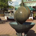 Schalenbrunnen_HD_16zu9.JPG Bronzener Schalenbrunnen in einer Fußgängerzone vor einem Café bei Sonnenschein.