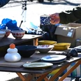 Flohmarkt.png Person hält eine blaue Tasse an einem Flohmarktstand mit bunten Keramiktellern und Schalen.