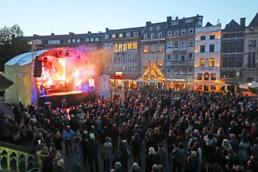 Auf dem Marktplatz ist eine Bühne aufgebaut, vor der viele Zuschauer*innen versammelt sind und einem Konzert lauschen.