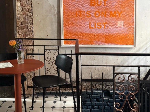 Small table with two chairs in front of a rough wall and a large orange text poster in the interior.