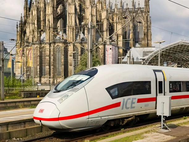 ICE am Bahnsteig vor großer gotischer Kathedrale mit Oberleitungen und Bahnhofsdach
