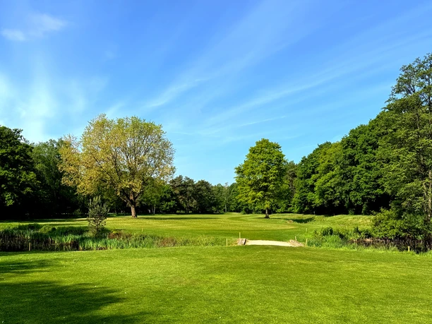Golf-Club GT Grüner Golfplatz mit Fairway, kleinem Steg und altem Baumbestand unter blauem Himmel