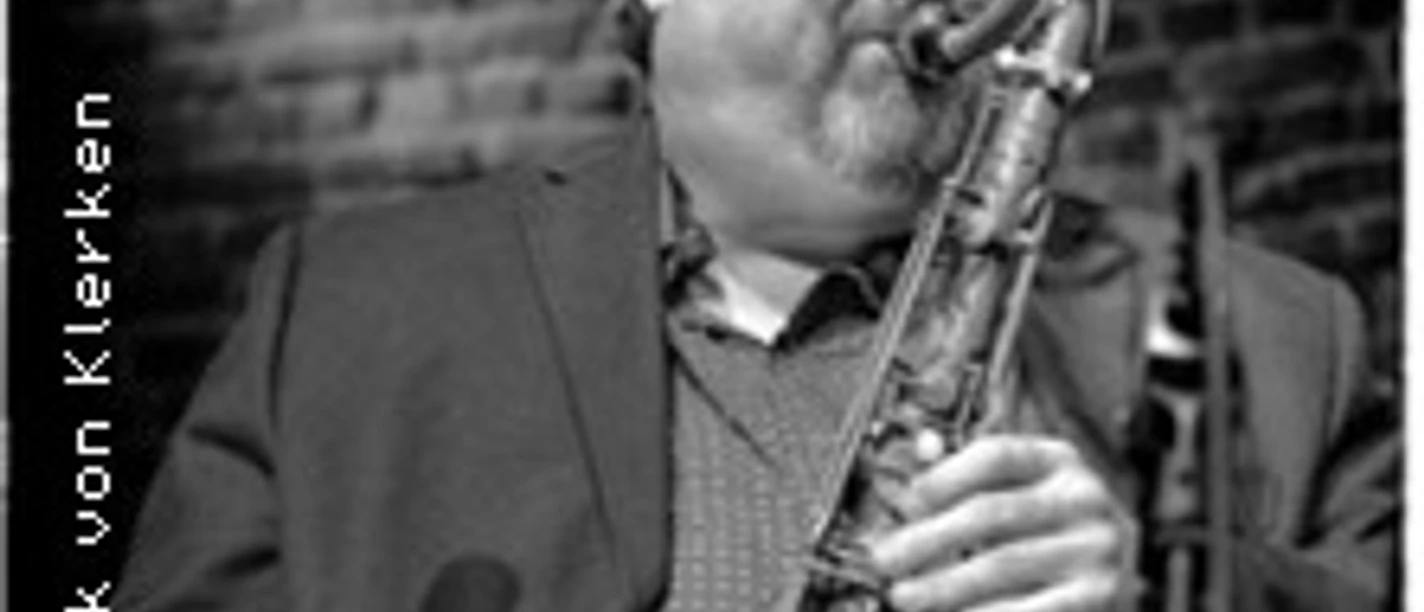 Ein Musiker spielt konzentriert Saxophon vor einer Backsteinwand in einer Schwarzweißaufnahme.