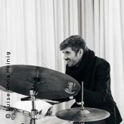 Schlagzeuger spielt konzentriert an einem Drumset vor hellen Vorhängen.