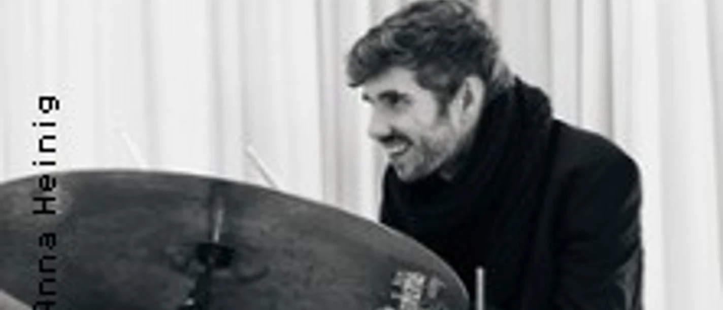 Schlagzeuger spielt konzentriert an einem Drumset vor hellen Vorhängen.