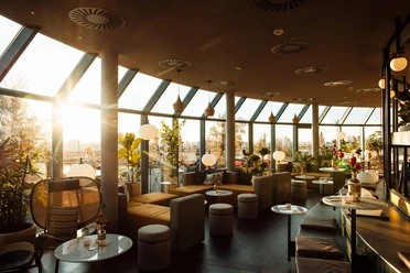 Sunset at the Bar Botanik Bright bar with large windows, plants and modern seating areas in the warm evening light