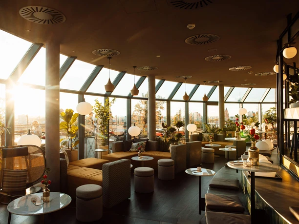 Sunset at the Bar Botanik Bright bar with large windows, plants and modern seating areas in the warm evening light