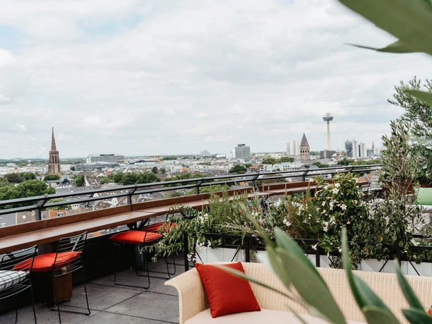 Bar Botanik - Rooftop Bar Rooftop terrace with seating, plants and sweeping views over the city and striking buildings