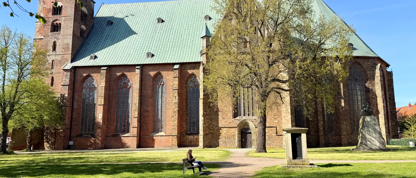 Dom Verden Großer Backsteindom mit grünem Dach und Turm. Davor Wiese und Bäume.