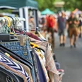 Flohmarkt Kleider auf Kleiderbügeln an einem Marktstand mit verschwommenen Menschen im Hintergrund