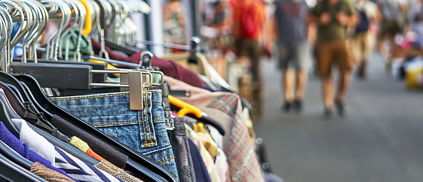 Flohmarkt Kleider auf Kleiderbügeln an einem Marktstand mit verschwommenen Menschen im Hintergrund