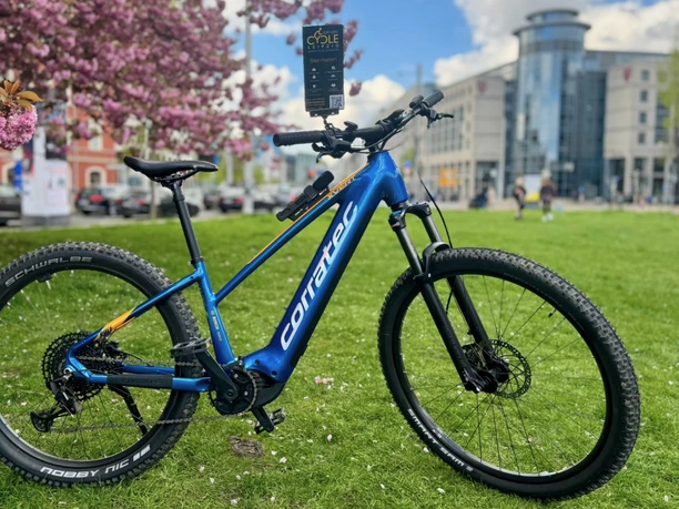 Modré horské kolo Cycle-Leipzig stojí před rozkvetlou třešní na náměstí Johannisplatz.