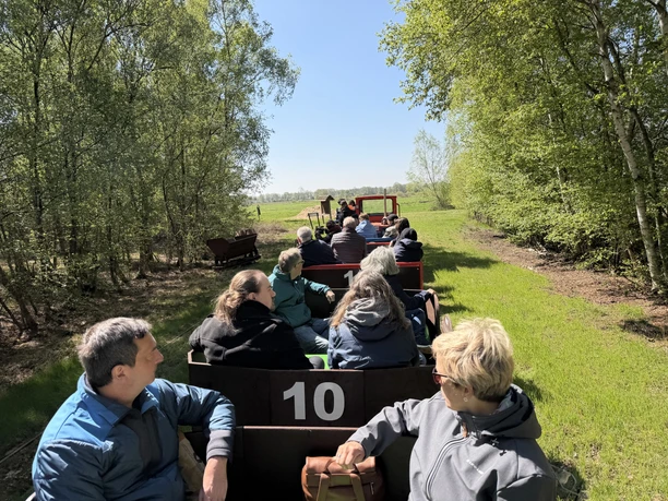 Uchter Moorbahn People in open carriages of the Uchter Moorbahn ride through a green landscape.