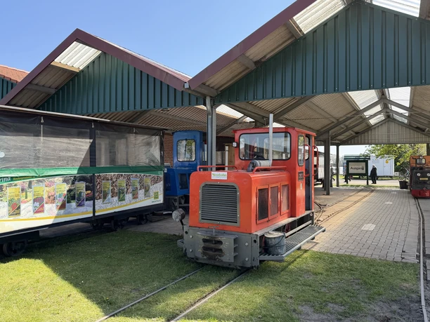 Red locomotive of the Uchter Moorbahn stands ready with carriages under a covered station track.
