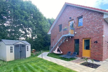 Vacation rental in a red brick house with an outdoor staircase, a garden, lounge chairs, and a small cabin.