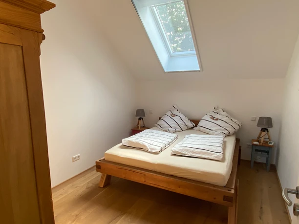 Gemütlich übernachten Helles Schlafzimmer mit Doppelbett aus Holz unter einem Dachfenster und Holzfußboden.