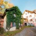 Tusculum @Tourist Information Murnau.jpg Das Bild zeigt das Christoph-Probst-Geburtshaus in Murnau.. Ein kleines Haus mit Efeu neben einem größeren Gebäude an einem herbstlichen Hof.