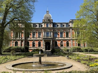 Red brick castle Etelsen with fountain in the park under a blue sky.