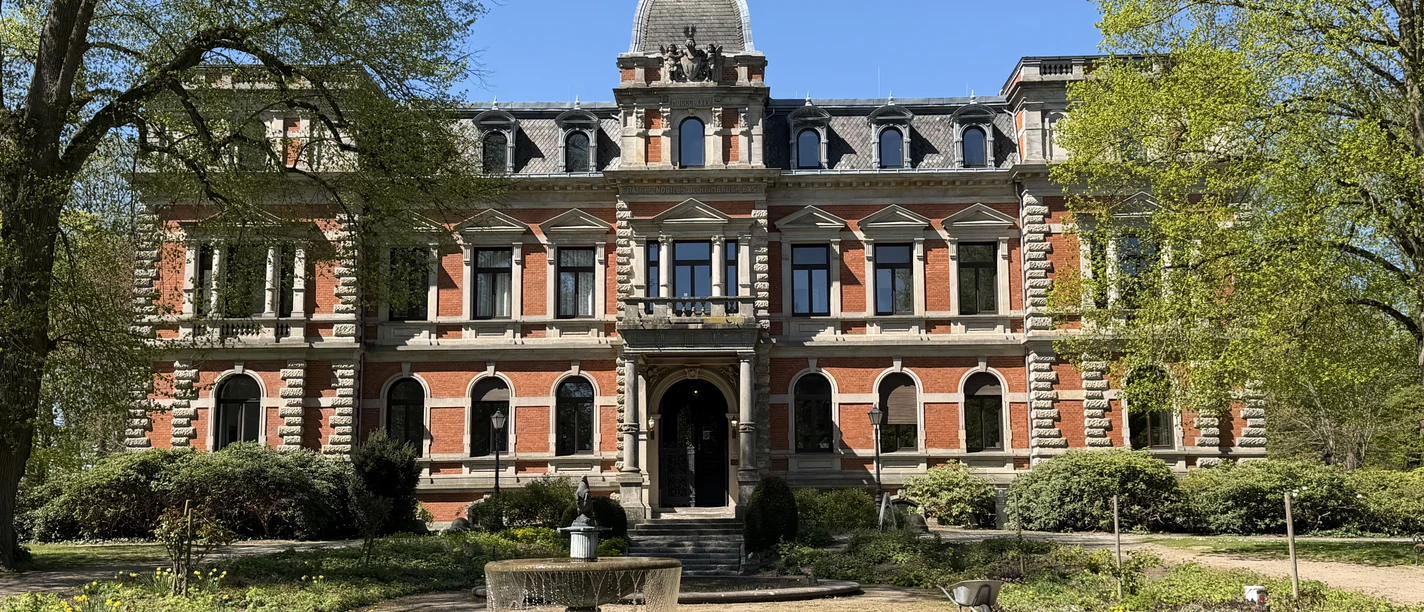 Schloss Etelsen Rotes Backsteinschloss Etelsen mit Springbrunnen im Park unter blauem Himmel.