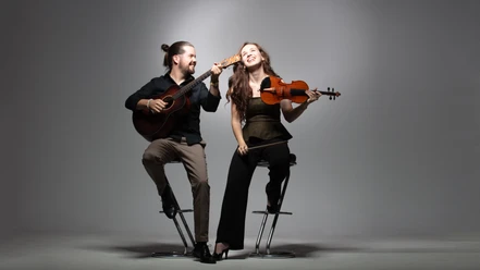 Festival aufm Platz Duo Lea Brückner und Gábor Ladányi Ein fröhliches Musiker-Duo auf Barhockern: Er spielt Gitarre, sie hält lächelnd eine Geige.
