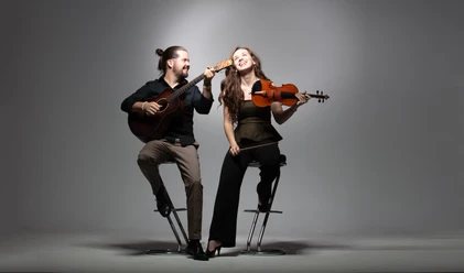 Brueckner_Ladanyi-1.jpg Ein fröhliches Musiker-Duo auf Barhockern: Er spielt Gitarre, sie hält lächelnd eine Geige.
