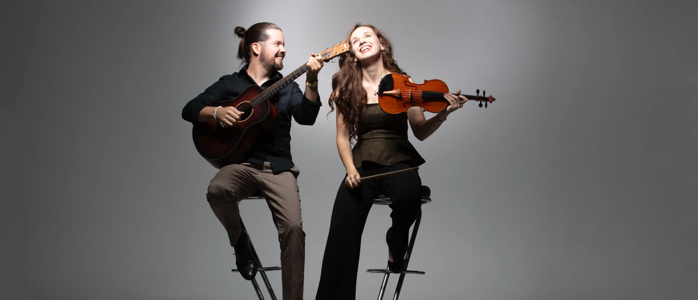 Brueckner_Ladanyi-1.jpg Ein fröhliches Musiker-Duo auf Barhockern: Er spielt Gitarre, sie hält lächelnd eine Geige.