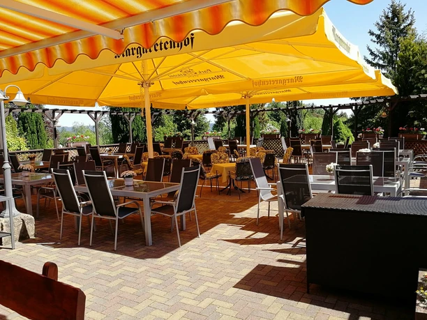 Gedeckte Tische und Stühle unter einem gelben Sonnenschirm in einem Außenbereich eines Restaurants.
