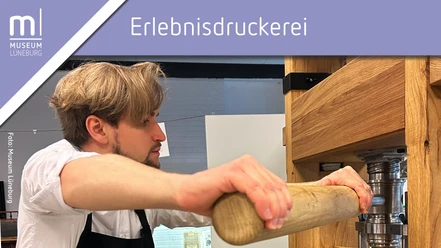 Schaudrucken in der Erlebnisdruckerei im Museum Lüneburg Ein Mann steht an der Druckerpresse und drückt einen Hebel aus Holz.