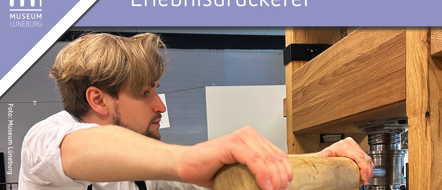 Schaudrucken in der Erlebnisdruckerei im Museum Lüneburg Ein Mann steht an der Druckerpresse und drückt einen Hebel aus Holz.