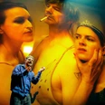 Schauspiel Köln - FAUST Ein Schauspieler steht vor einer großen Projektion mit drei intensiv spielenden Bühnenfiguren.
