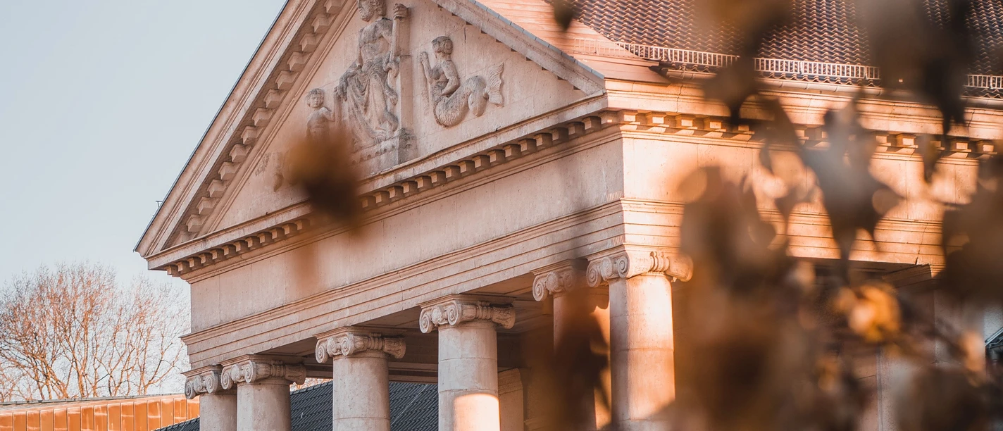 Im Morgenlicht steht das Kurhaus Aachen vor unscharf gestellten Blättern eines Baumes.