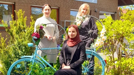 Radlertreff_SHS_Mai2026.jpg Drei Frauen vor Backsteingebäude mit blauem Fahrrad und Blumendeko