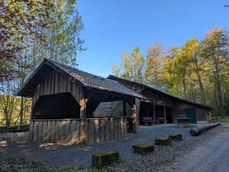 Grillhütte, Vardeilsen, Panoramaweg, CC0 (2).jpg Hölzerne Grillhütte mit Ziegeldach am sonnigen Waldrand, davor ein Schotterplatz mit Bänken.