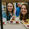 Kulinarischen Schnitzeljagd Zwei Personen greifen bei einer Verkostung nach kleinen Häppchen auf Papptellern.