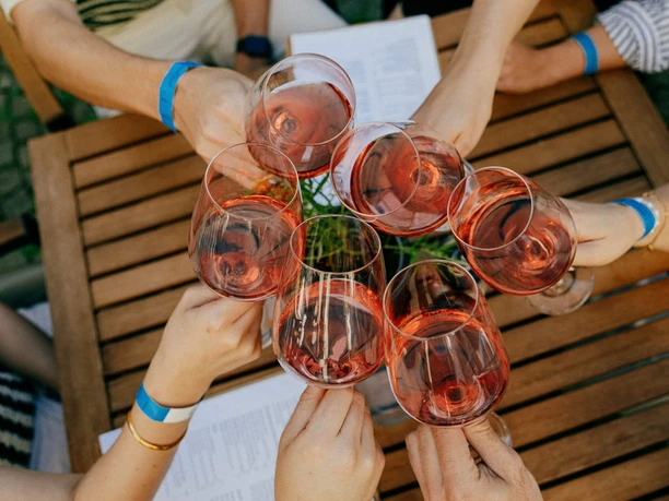 Several hands clink glasses of rosé over a wooden table