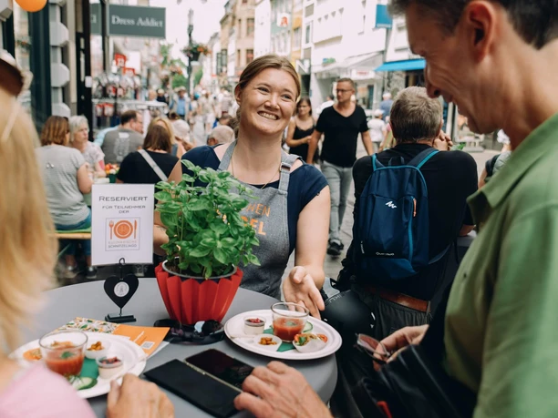 Culinary scavenger hunt Smiling service staff handing out appetizers at a busy street table at a food event.