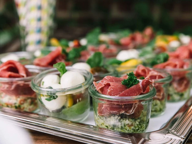 Culinary scavenger hunt Small glasses with antipasti of mozzarella, vegetables and finely sliced ham on a tray.