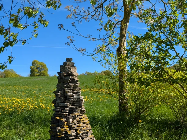 Bank, Rastplatz, steinerne Türme Kuhlager, Panoramaweg Geschichteter Steinturm auf einer grünen Wiese mit gelben Blumen vor blauem Himmel.