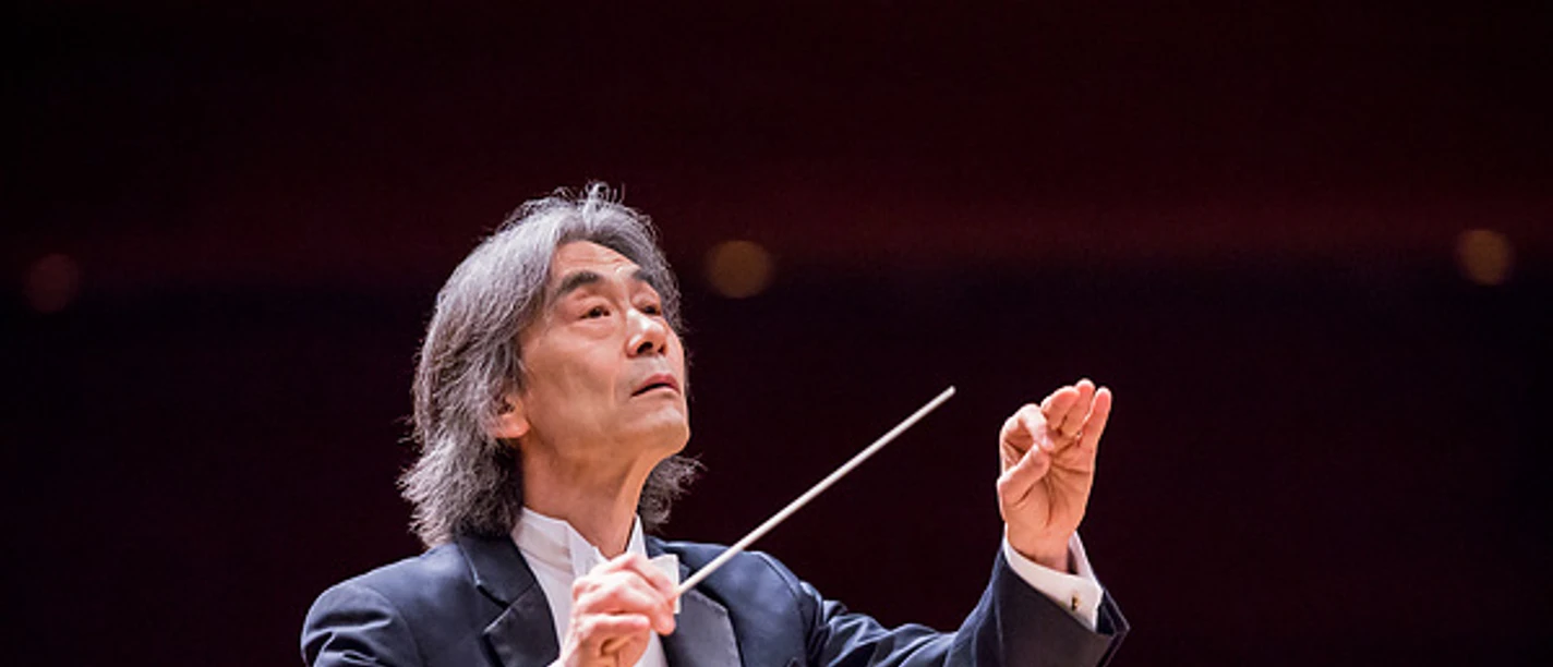 Nagano, Kent A conductor in a tailcoat leads an orchestra with a raised baton in a concert hall