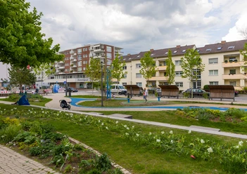 Spieplatz Große Kirche S7300 (c) Helmut Gross_Erlebnis Bremerhaven_WEB.jpg Grüner Spielplatz kirchPARK mit blauem Pfad, Pflanzen und Sitzbänken vor Wohngebäuden.