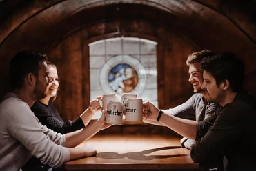 Einbecker_Brauhaus_Fass.jpg Vier Personen stoßen lachend mit Einbecker Krügen an. In diesem großen Fass feiert ihr mit!