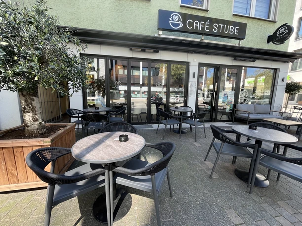 Außenterrasse der Café Stube mit Tischen, schwarzen Stühlen und Glasfront