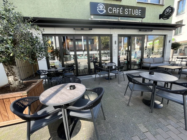 Außenterrasse mit Tischen und Stühlen vor dem Café Stube mit großer Glasfront und Markise