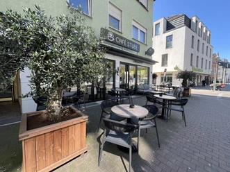 Café Stube Außenterrasse der Café Stube mit Tischen, Stühlen und Olivenbaum vor dem Eingang
