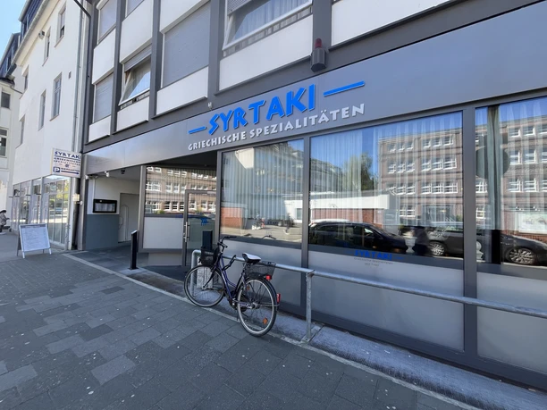 Außenansicht des Restaurants Syrtaki mit großer Fensterfront und Fahrrad davor