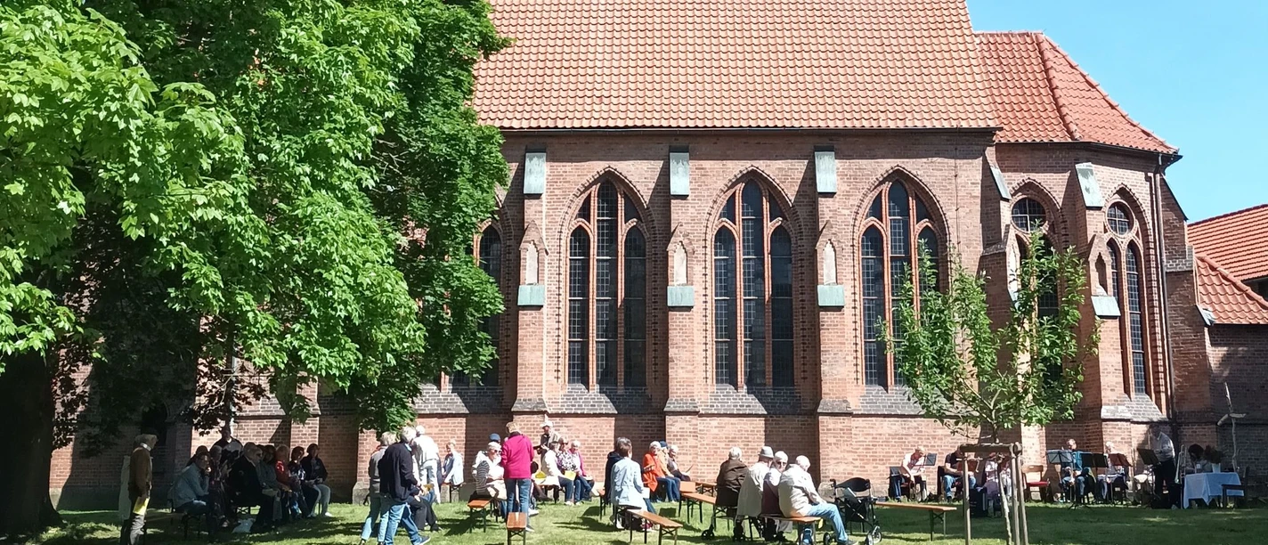 Kirche_Ohlendorf_Himmelfahrt_HD_16zu9.jpg Freiluftgottesdienst: Menschen auf Bänken und ein Posaunenchor vor einer roten Backsteinkirche.