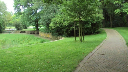 Terrainkurwege_SZ-Bad_HD_16zu9.JPG Gepflasterter Kurweg schlängelt sich durch eine grüne Parkanlage mit Bäumen und Sitzbänken.