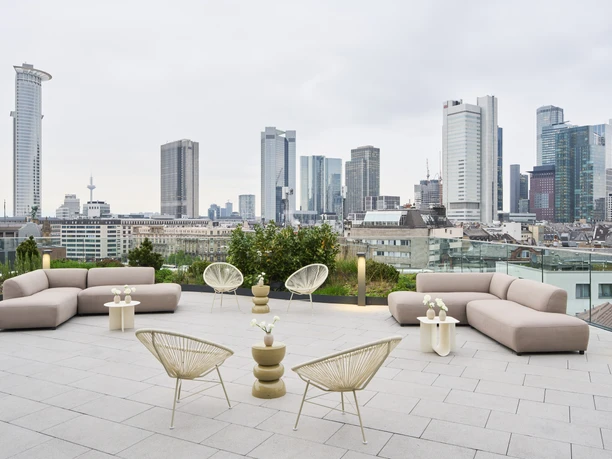Kreisler - 2 Moderne Dachterrasse mit Loungemöbeln und weitem Panoramablick auf die Frankfurter Skyline unter bewölktem Himmel.