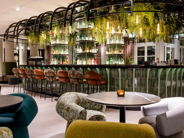 Motel One Frankfurt-Hauptbahnhof - Hotelbar Moderne Hotelbar im Motel One Frankfurt-Hauptbahnhof mit grünen Akzenten, hängenden Pflanzen und stilvollen Barhockern.